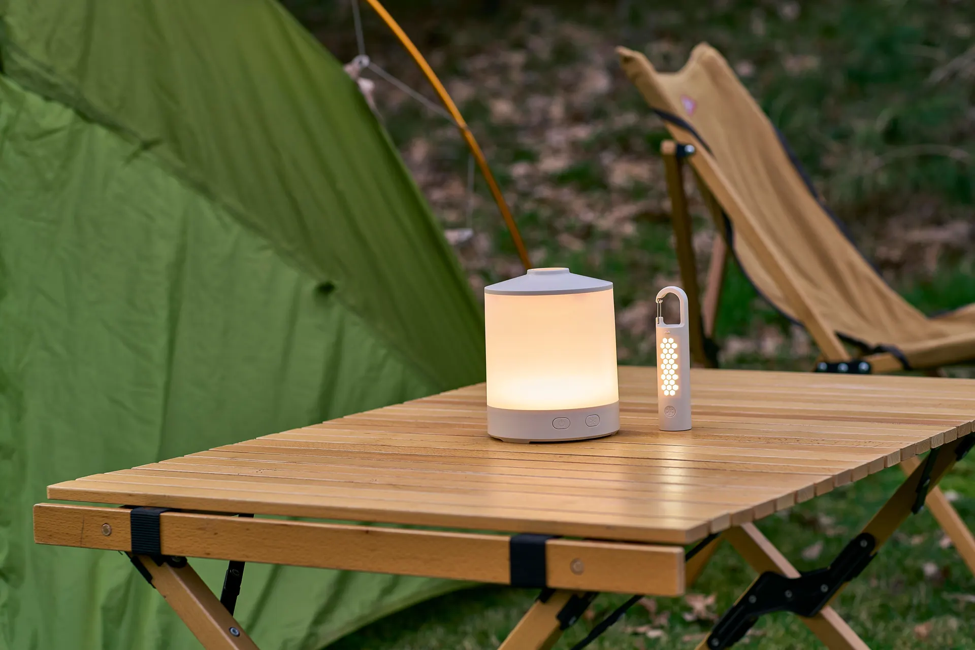 Campinglampe und Taschenlampe auf einem Holztisch vor Zelt und Campingstuhl